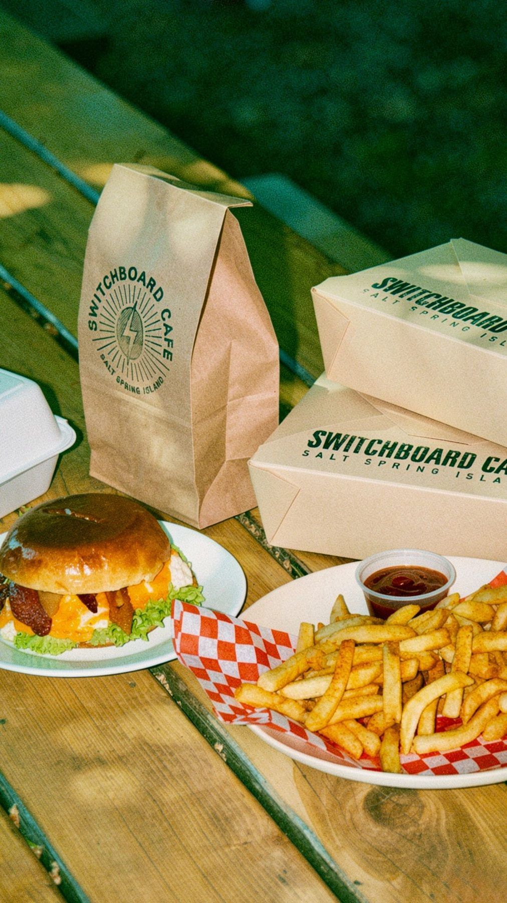 A Switch burger and fries on the patio table, with a stamped takeout bag and boxes
